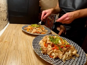A naked gay chef prepares a dish of rice noodles with chicken and vegetables.